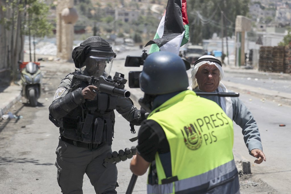 After a demonstration against Israeli settlements in the occupied West Bank village of Beita, a member of the Israeli army points a tear gas launcher and pushes away a Palestinian protester while a journalist is filming, on 18 June 2021 (AFP)