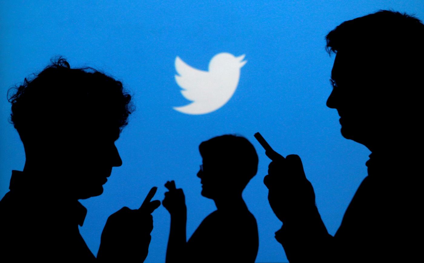 People are silhouetted against a backdrop projected with the Twitter logo (Reuters)
