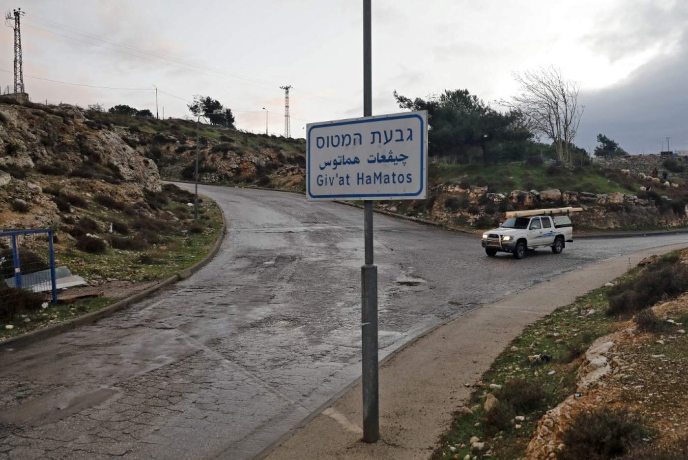A car advances on a road, by a street placard signaling entry into Givat Hamatos, an Israeli settlement suburb of annexed east Jerusalem, 15 November 2020 (AFP)