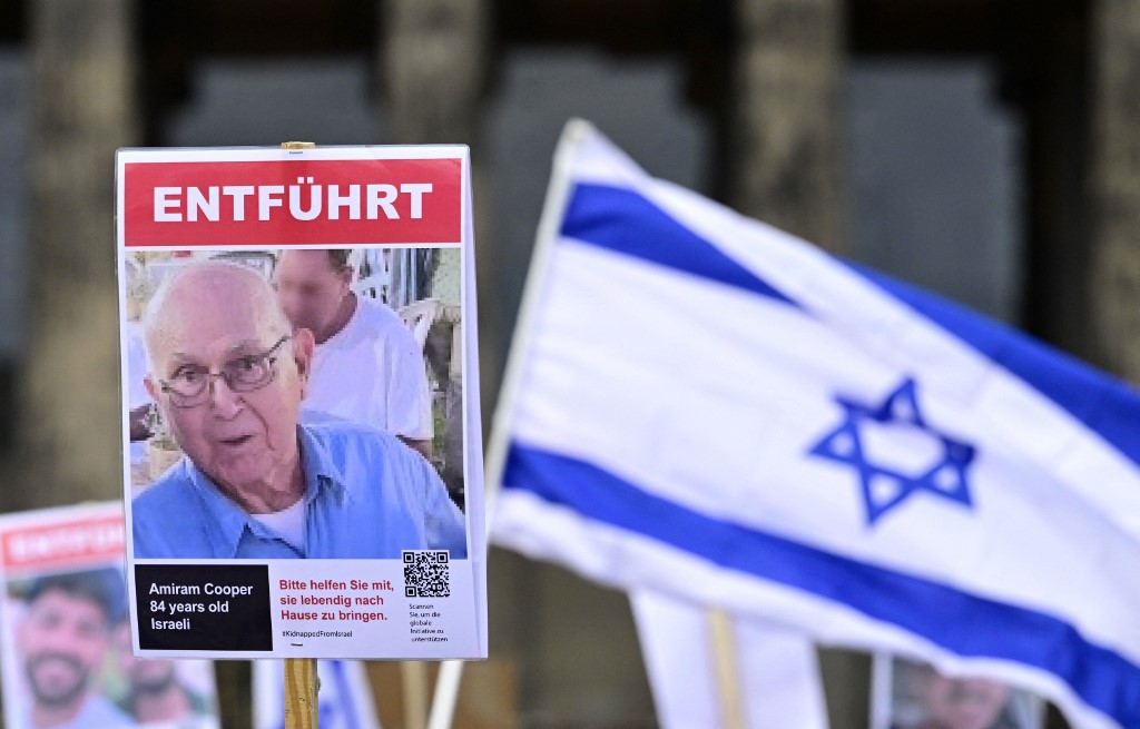 Demonstrators wave an Israeli flag and hold a placard with the portait of late Israeli hostage Amiram Cooper on January 14, 2024 in Berlin (John MacDougall / AFP)