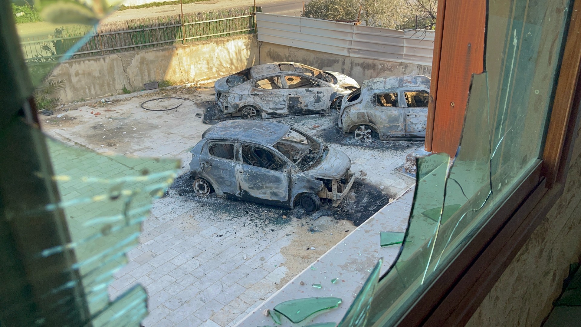 Cars burnt out by settlers are seen from a broken window in occupied West Bank town Huwwara on 27 February 2023. (Photos: MEE/Hisham Abu Shaqrah)