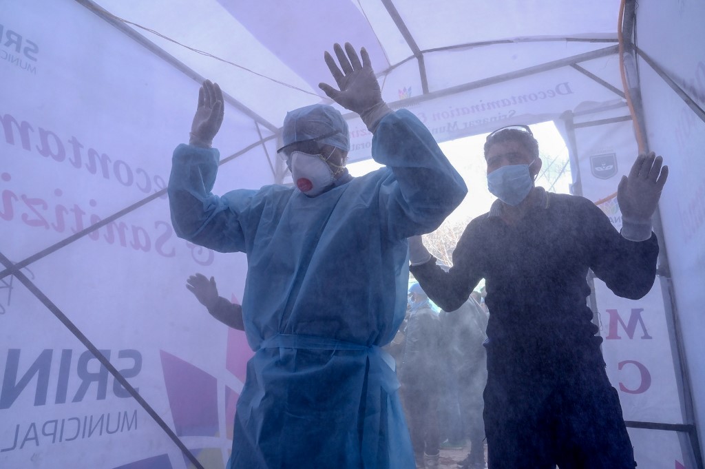 Medical staff walk through a disinfecting tunnel before entering a hospital in Srinagar on 2 April (AFP)