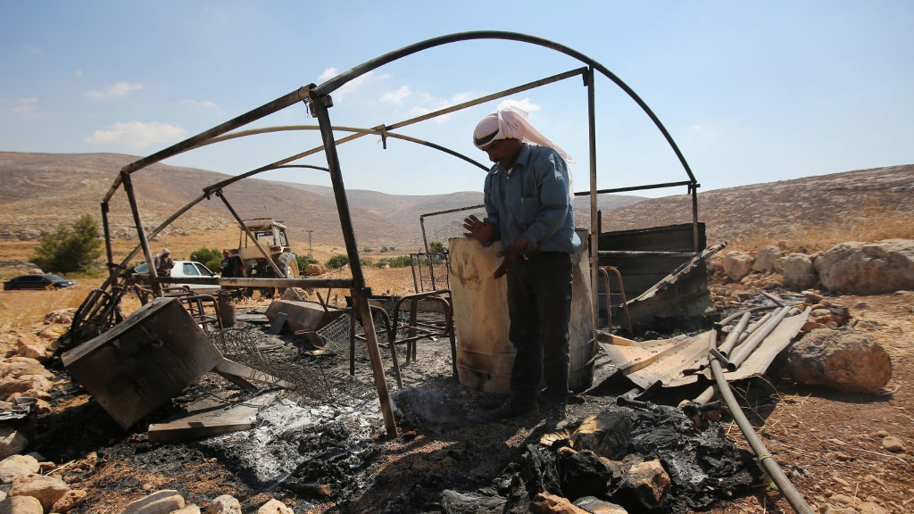 Un bédouin palestinien examine une tente incendiée à Ein Samia, en Cisjordanie occupée par Israël, après une attaque présumée de colons juifs en août 2015 (AFP)
