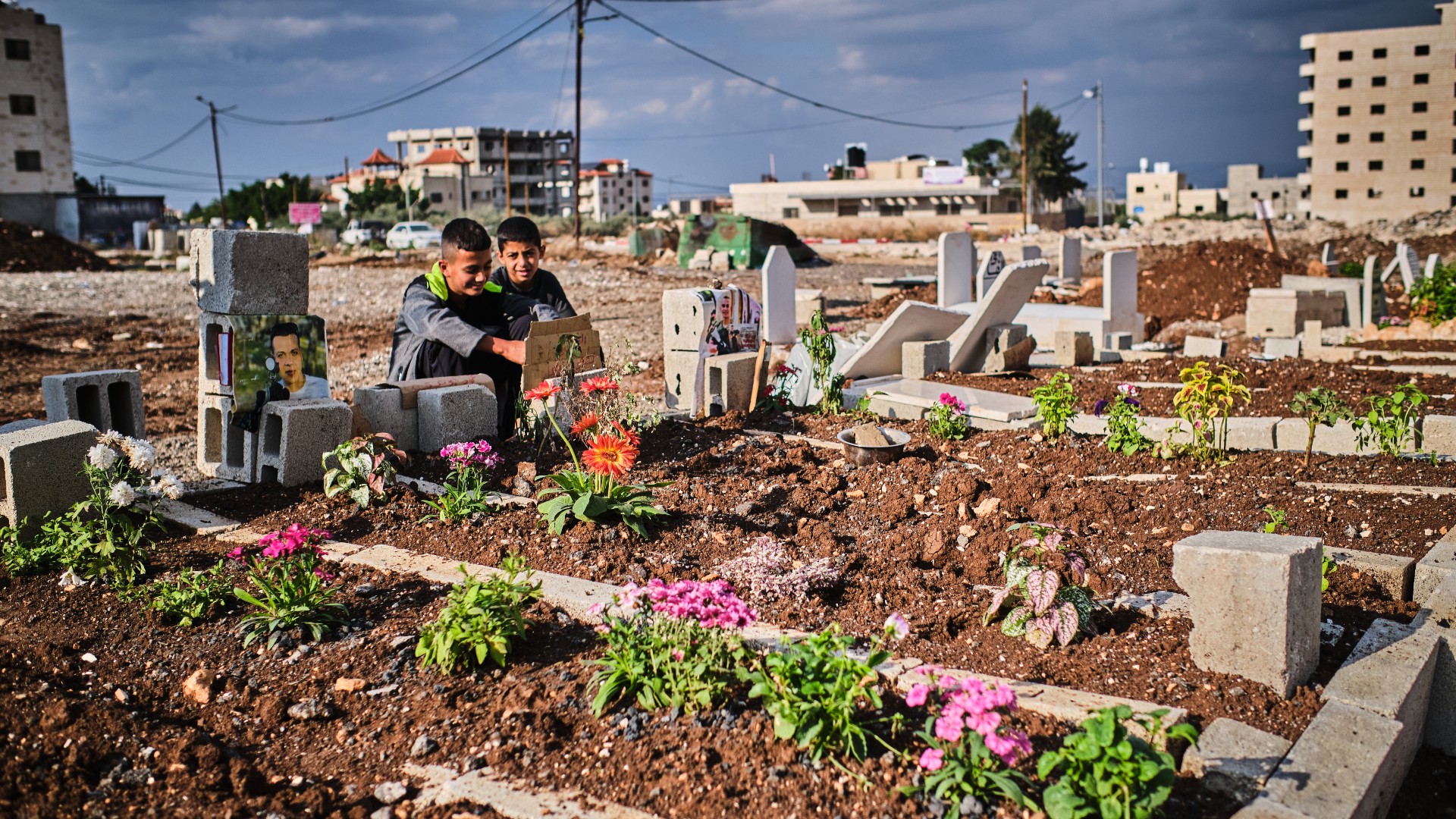 Children sit near the grave of a loved one at one of Jenin's sprawling graveyards (MEE/Angelo Calianno)