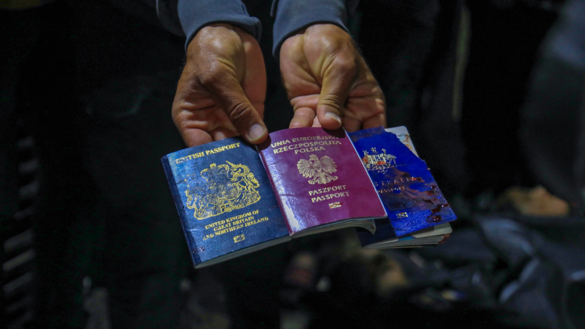 A man displays British, Polish, and Australian passports next to the bodies of World Central Kitchen workers at Al-Aqsa Hospital in Deir al-Balah, Gaza Strip, on 1 April 2024 (AFP)