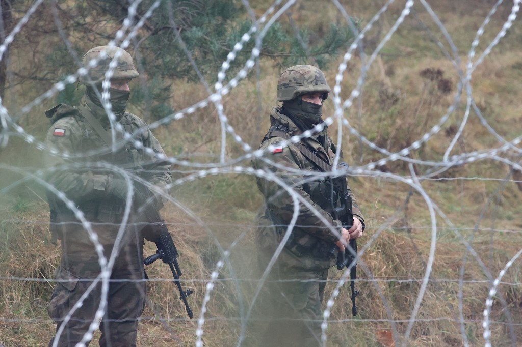 Polish forces stand by a fence on the Belarus border, as hundreds of refugees camp out in freezing temperatures in November 2021 (AFP)
