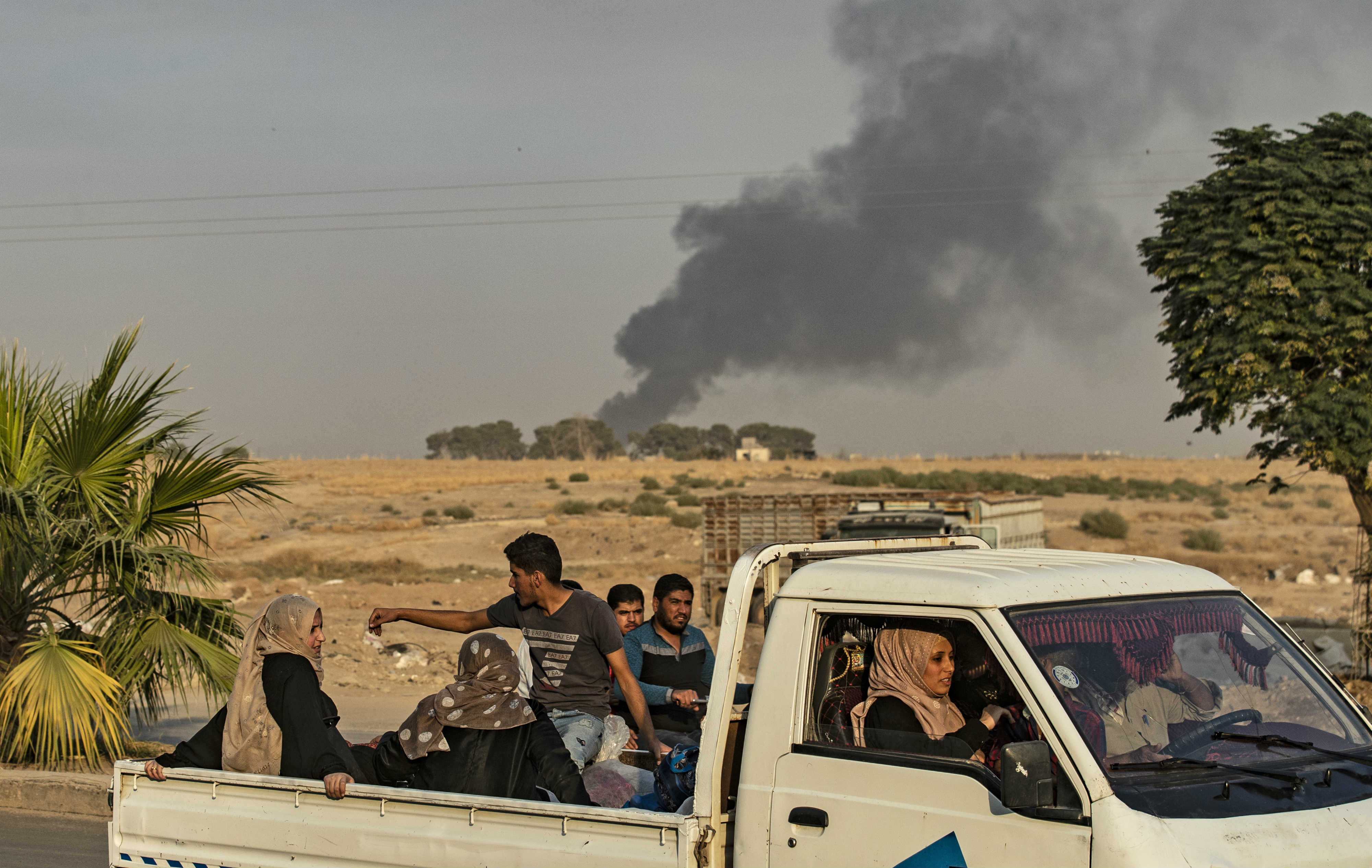 Syrians ride a pickup truck past smoke as civilians flee a Turkish bombardment near the town of Ras al-Ain (AFP)