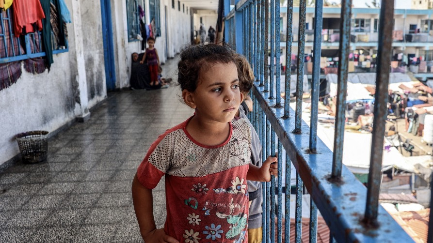 Children stand behind the rail of a hallway balcony outside classrooms sheltering displaced people at a Unrwa school in Gaza's Deir al-Balahon 9 September (Eyad Baba/AFP)