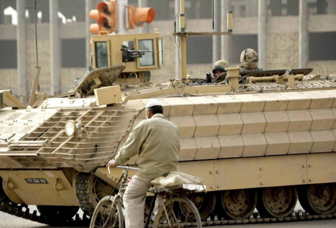 Un homme passe en vélo à côté d’un véhicule blindé britannique près du site d’un attentat à la bombe sur le bord d’une route à Bassorah, en février 2007 (AFP)