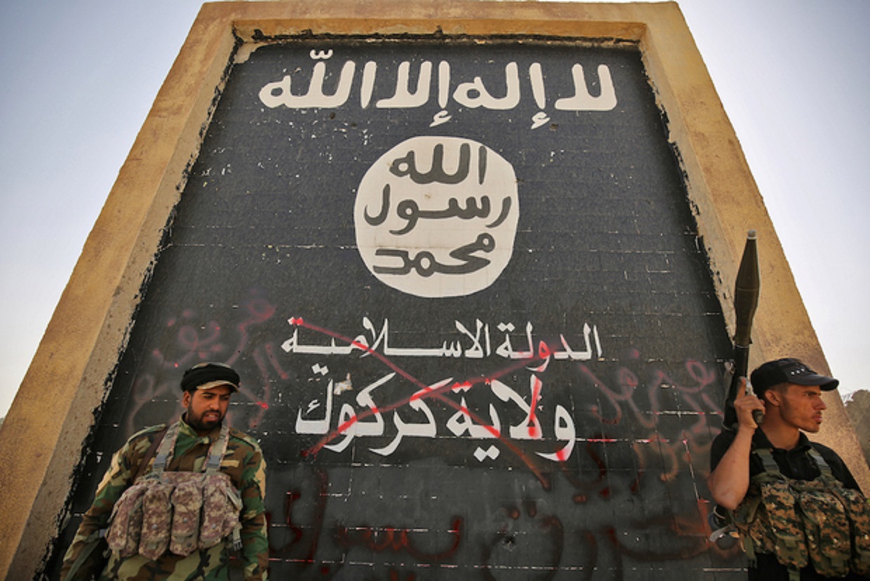 Des combattants soutenant les forces irakiennes se tiennent devant une peinture murale de l’EI alors que les troupes avancent dans Hawija le 5 octobre 2017, après avoir repris la ville au groupe (AFP)