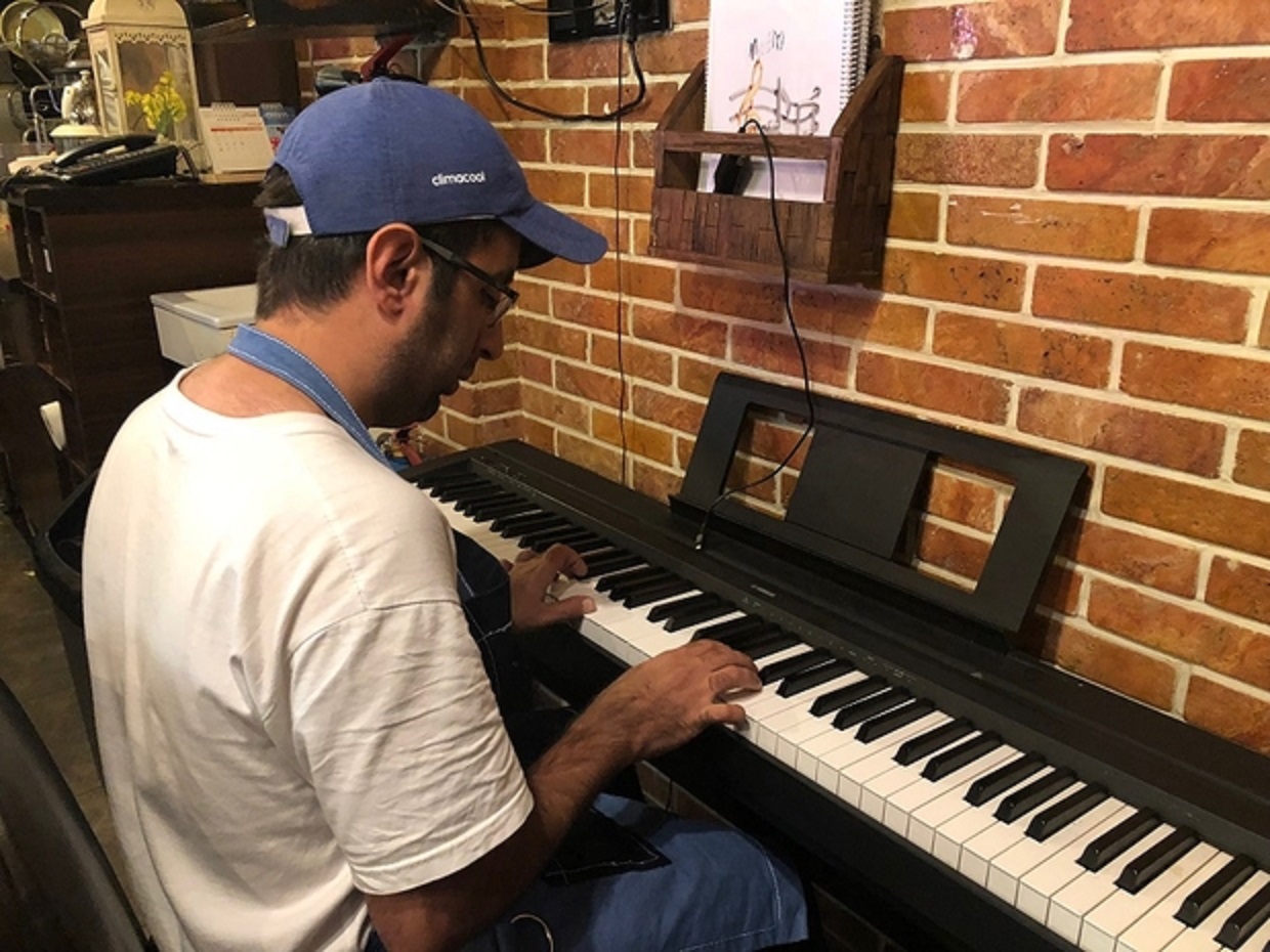 Mehdi Khakyan joue du piano au café Downtism à Téhéran, où les talents musicaux du personnel sont encouragés (MEE/Sahar Esfandiari)