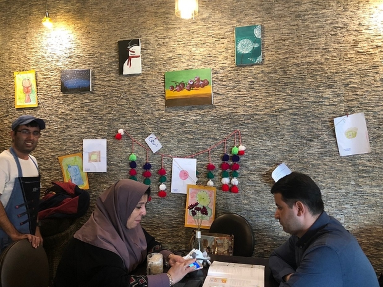 Mehdi Khakyan se tient derrière deux clients au café Downtism (MEE/Sahar Esfandiari)
