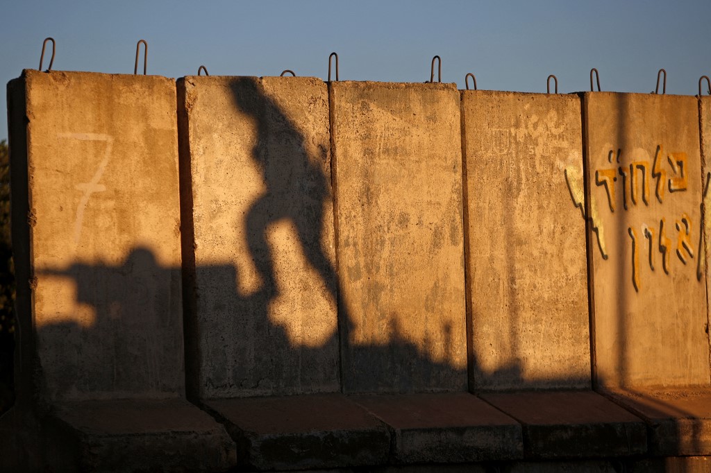 The shadow of an Israeli soldier climbing on a tank is seen on barricades along the northern border with Lebanon on 19 May 2021 (AFP)