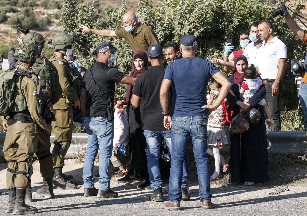Palestinians are blocked by Israeli policemen and army soldiers, some clad in masks due to the COVID-19 coronavirus pandemic, while on their way home at the entrance of a junction by the Palestinian village of Halhul, north of Hebron