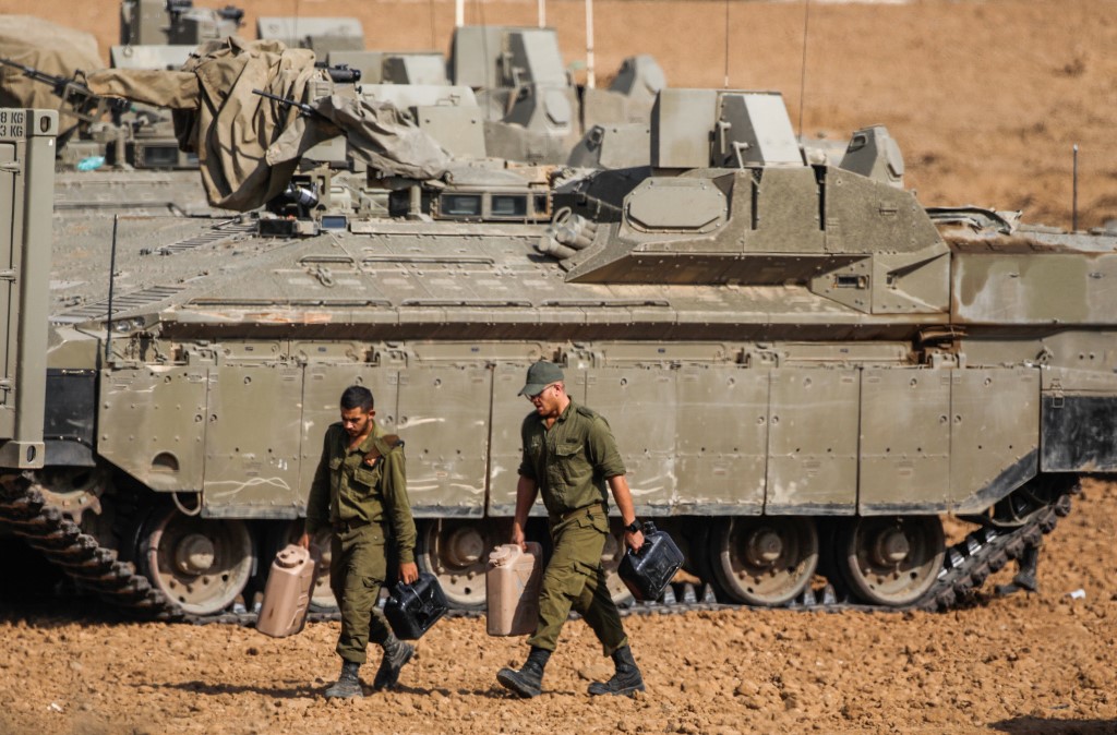 Israeli soldiers walk next to armoured vehicles near Gaza on 13 November (AFP)