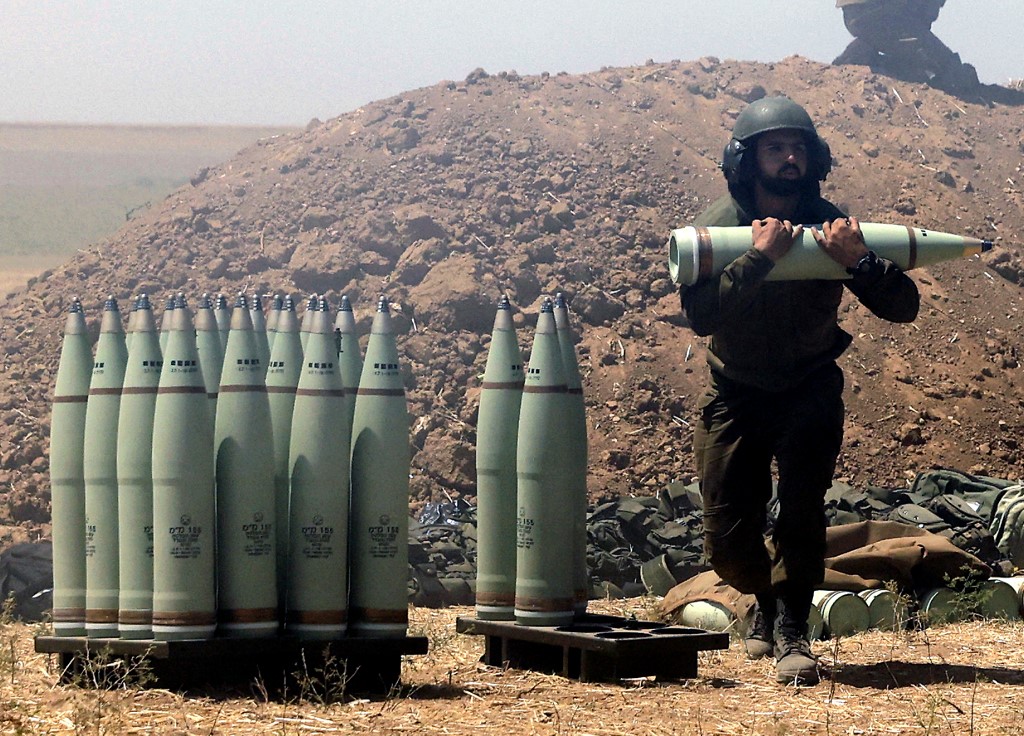 An Israeli soldier carries artillery shells to be fired towards Gaza on 19 May 2021 (AFP)