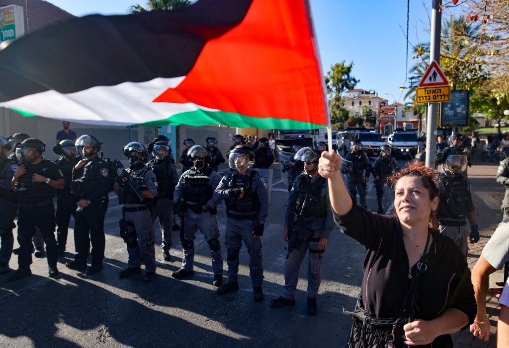 A woman raises a Palestinian flag in front of Israeli forces during a protest in Jaffa on 15 May 2021 (AFP)