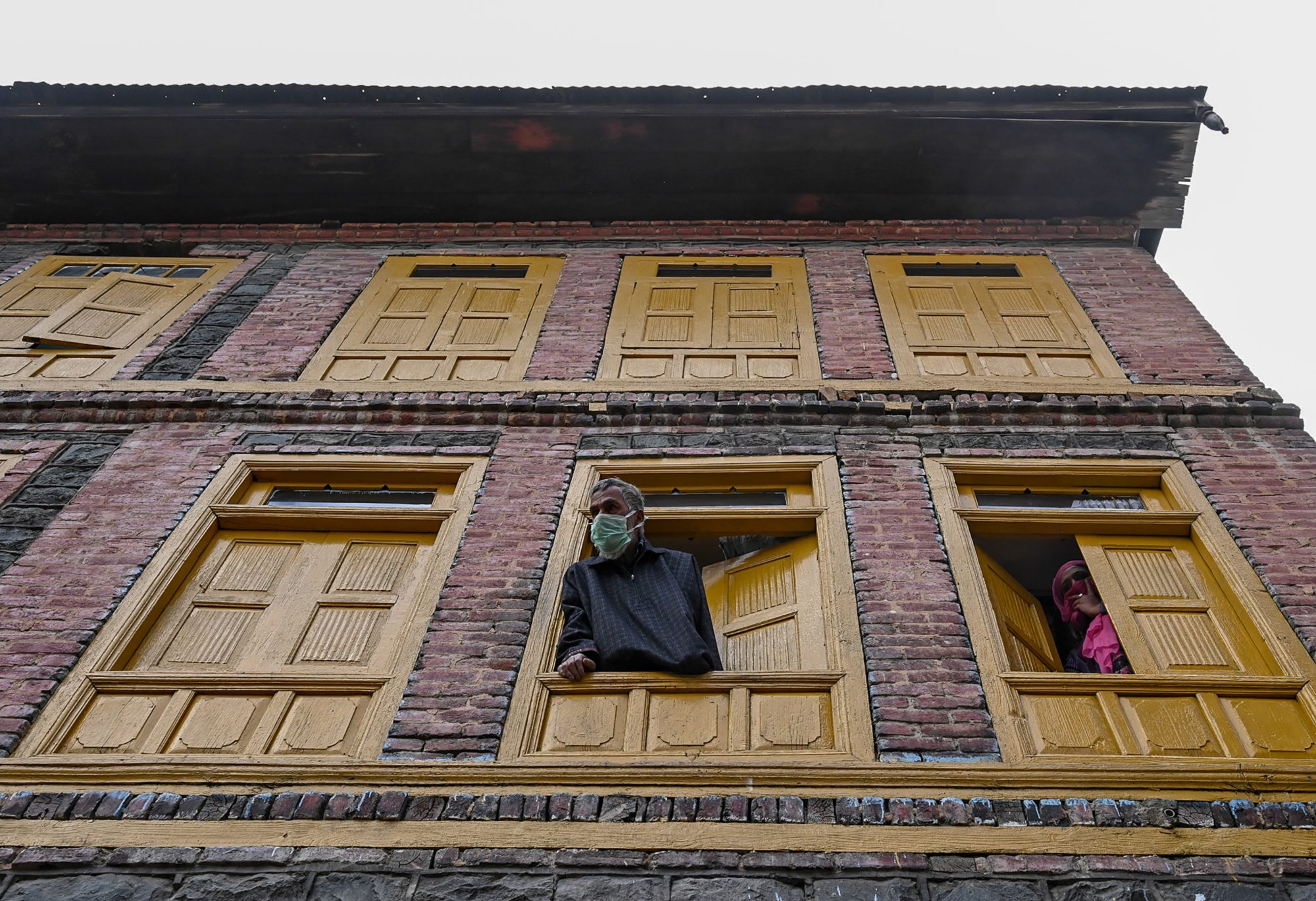 People look out from their windows in a residential area of Srinagar declared as a 'red zone' for coronavirus by authorities on 8 April 2020 (AFP)