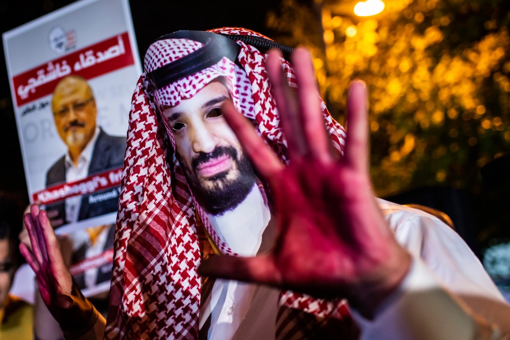 A protester wears a mask of Saudi Crown Prince Mohammed bin Salman amid posters of journalist Jamal Khashoggi during a 2018 demonstration in Istanbul, Turkey (AFP)