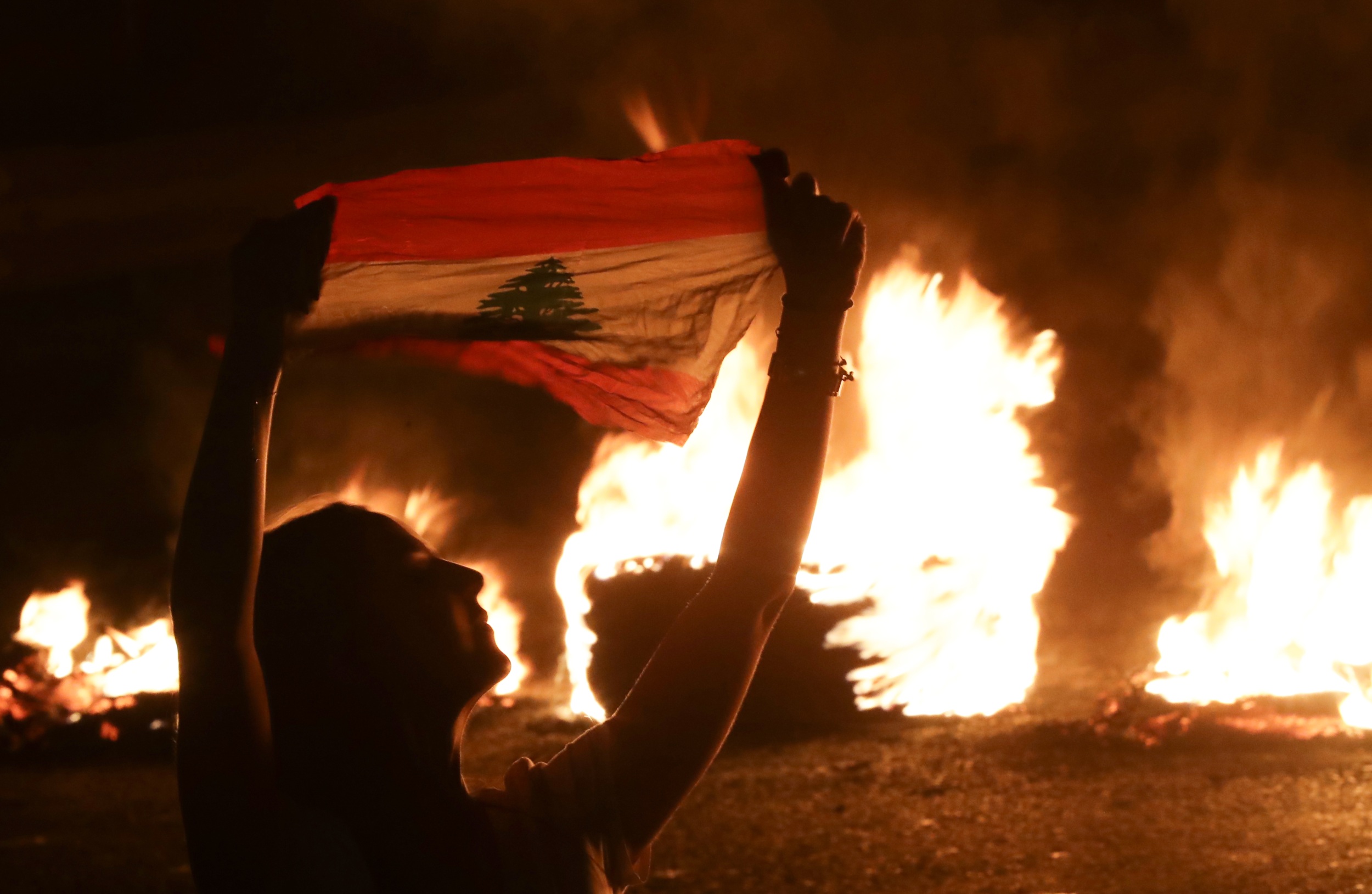 A Lebanese anti-government protester in front of burning tyres blocking the main highway linking the city of Tripoli to Beirut at the coastal city of Byblos, on 13 November 2019 (AFP)