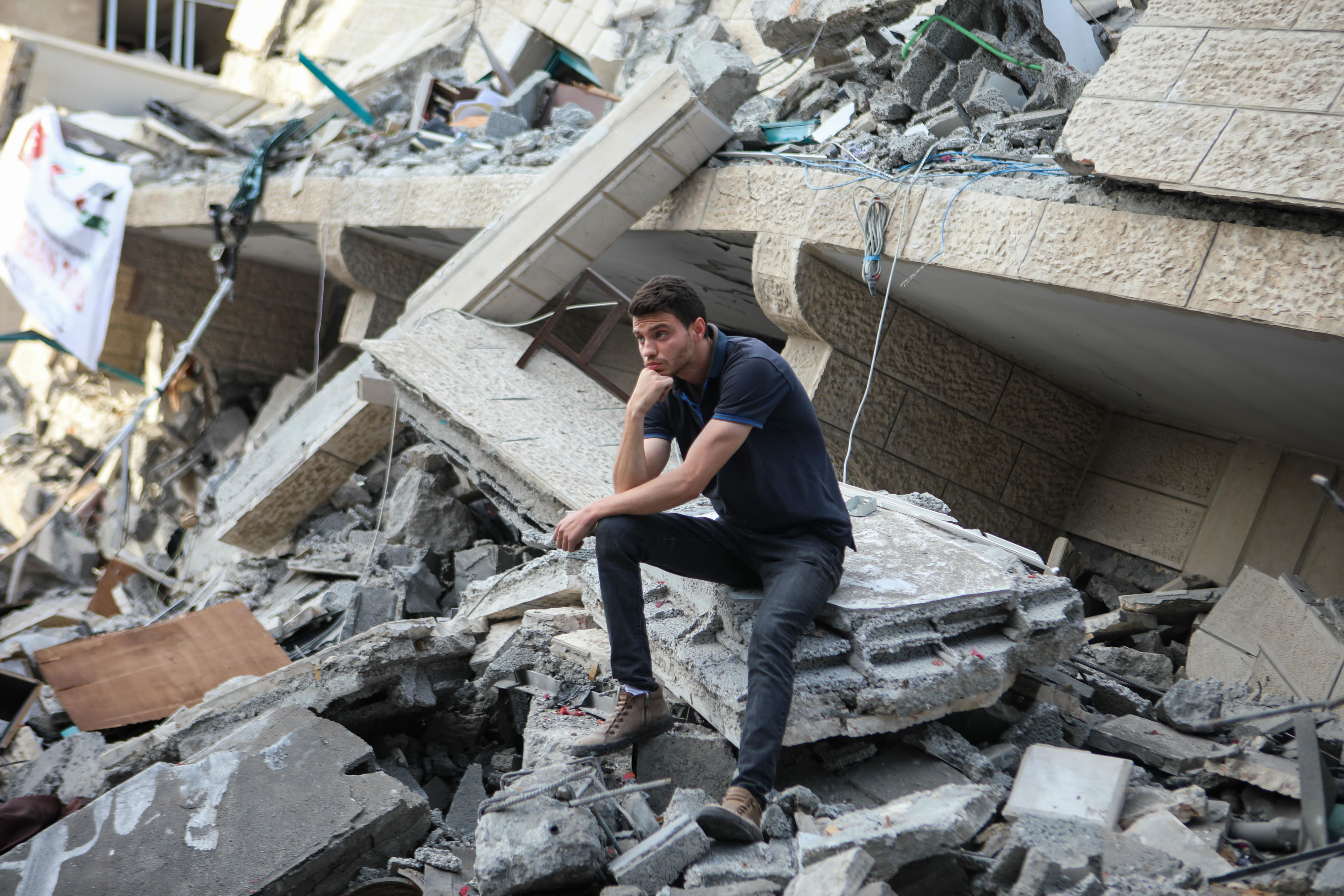 A Palestinian man sits on the rubble of a building demolished by Israeli strikes (MEE/Mohammed al-Hajjar)
