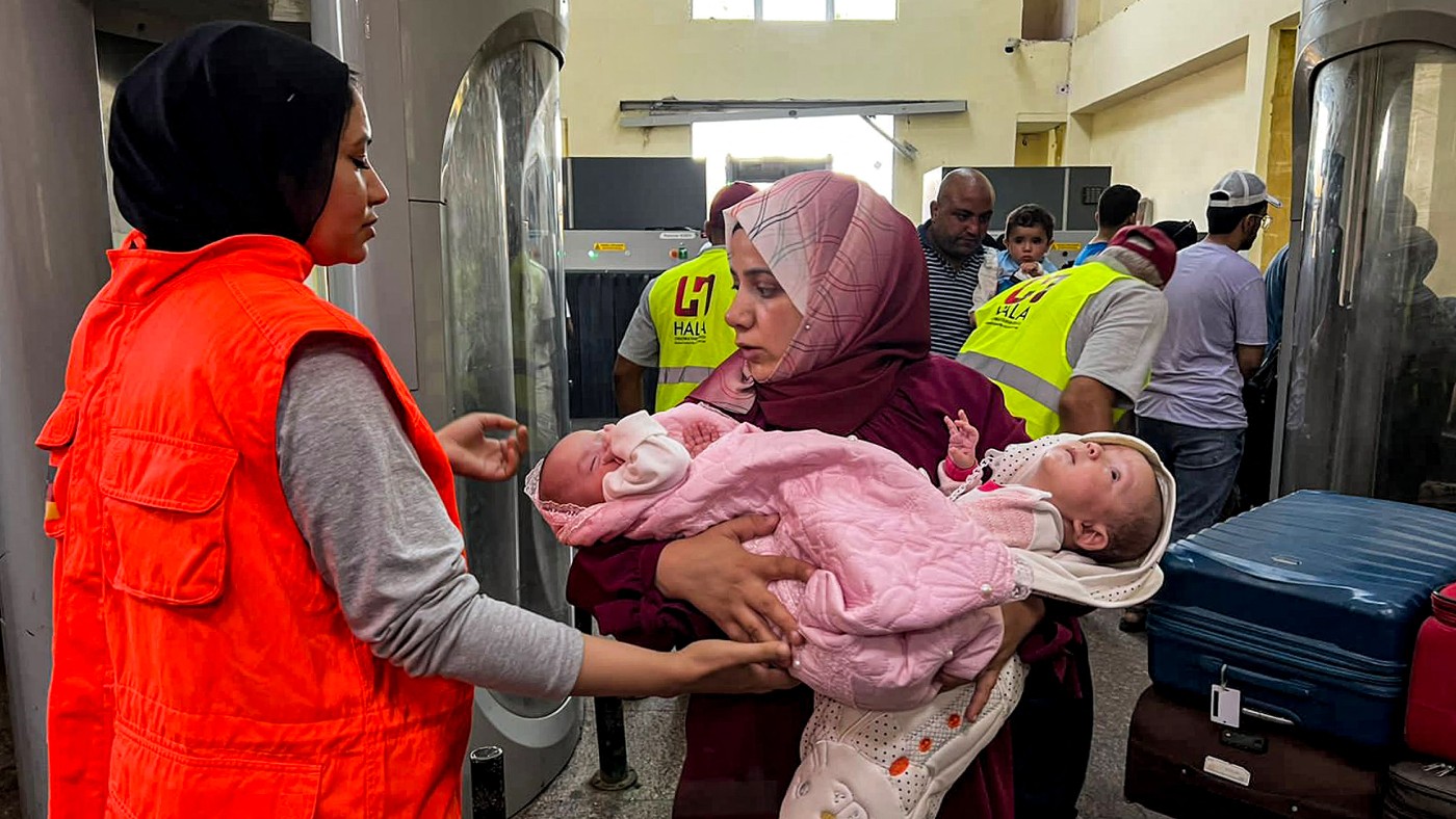 Une femme porte deux enfants en bas âge après être passée du côté égyptien du poste-frontière de Rafah avec la bande de Gaza, le 6 novembre 2023 (AFP)