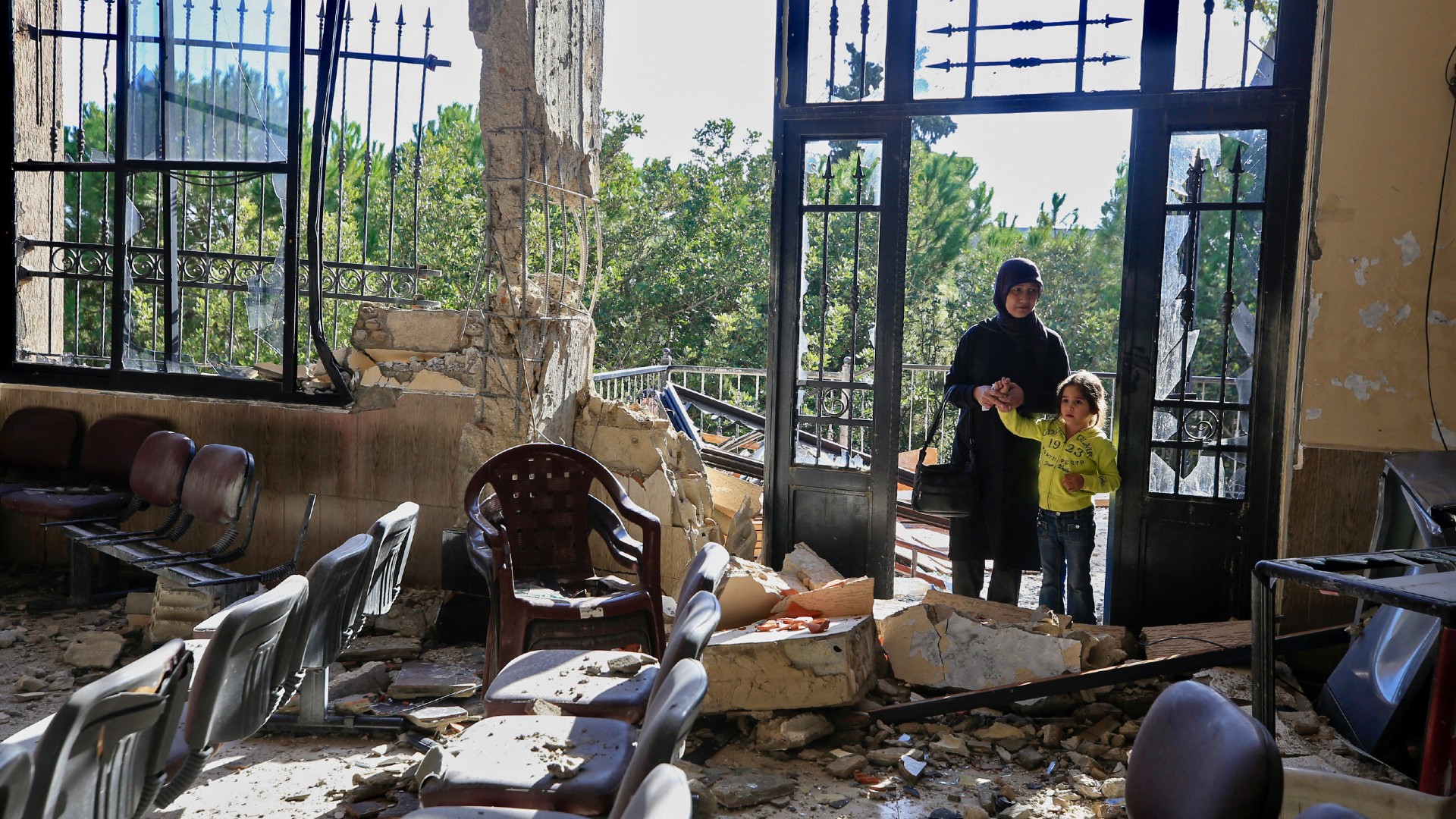 A woman and child stand at the entrance of a damaged building in the southern Lebanese village of Mhaybeeb following an Israeli strike on 24 November, 2023 (AFP)