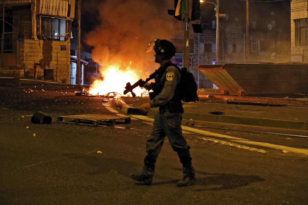 A member of Israel’s security forces passes burning barricades in the Shuafat refugee camp in occupied East Jerusalem on 14 May 2021 (AFP)