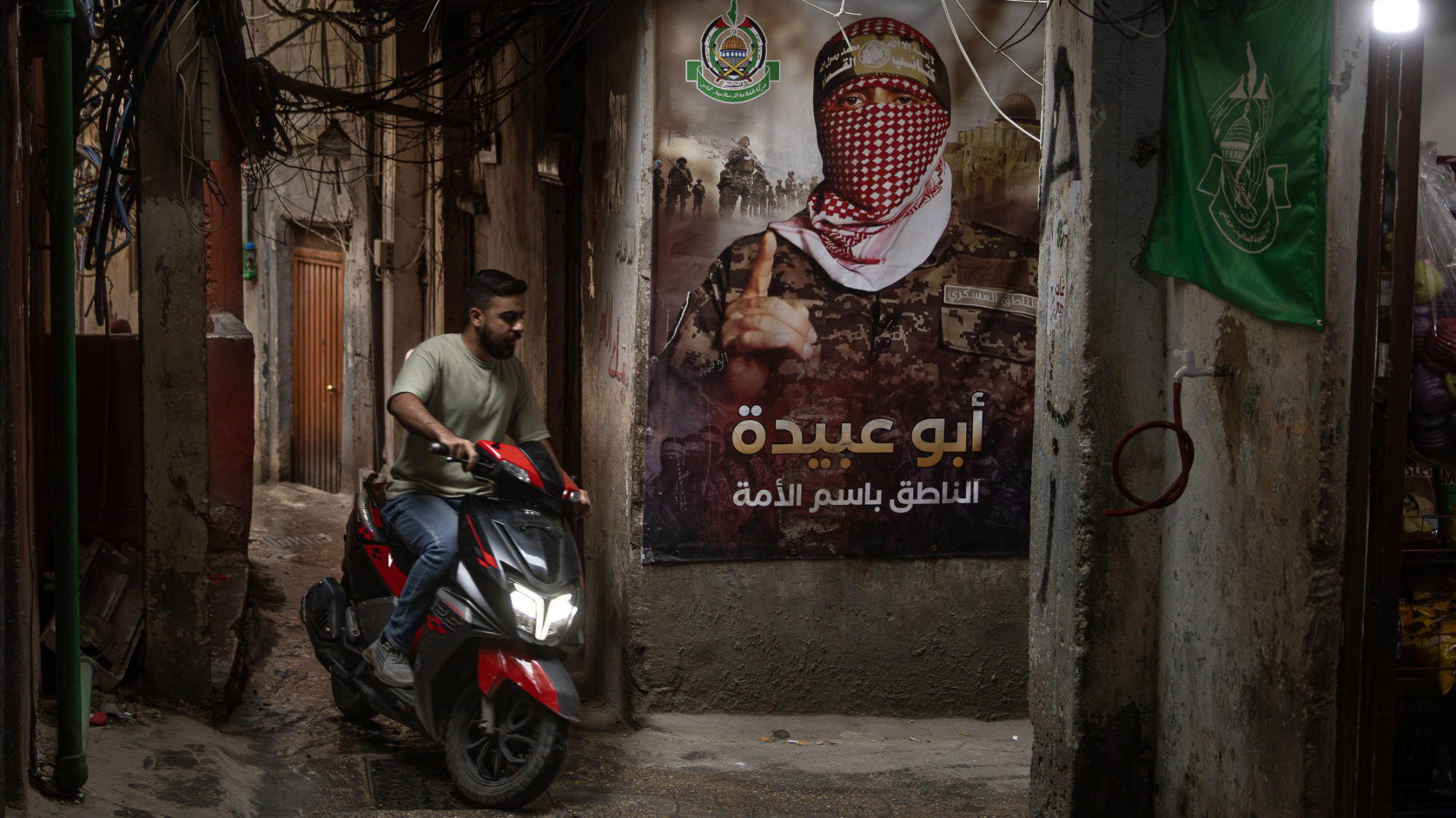 A man rides a motorcycle by a poster of Abu Obeida in Bourj el-Brajneh refugee camp for Palestinian refugees in Lebanon's Beirut on 18 May 2024 (Collin Mayfield/Sipa USA via Reuters) 