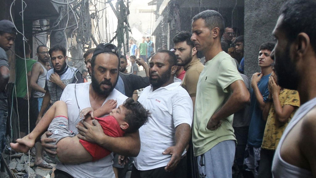 A Palestinian man carries a child in his arms after an Israeli air strike in Gaza City on 12 October 2023 (AFP)