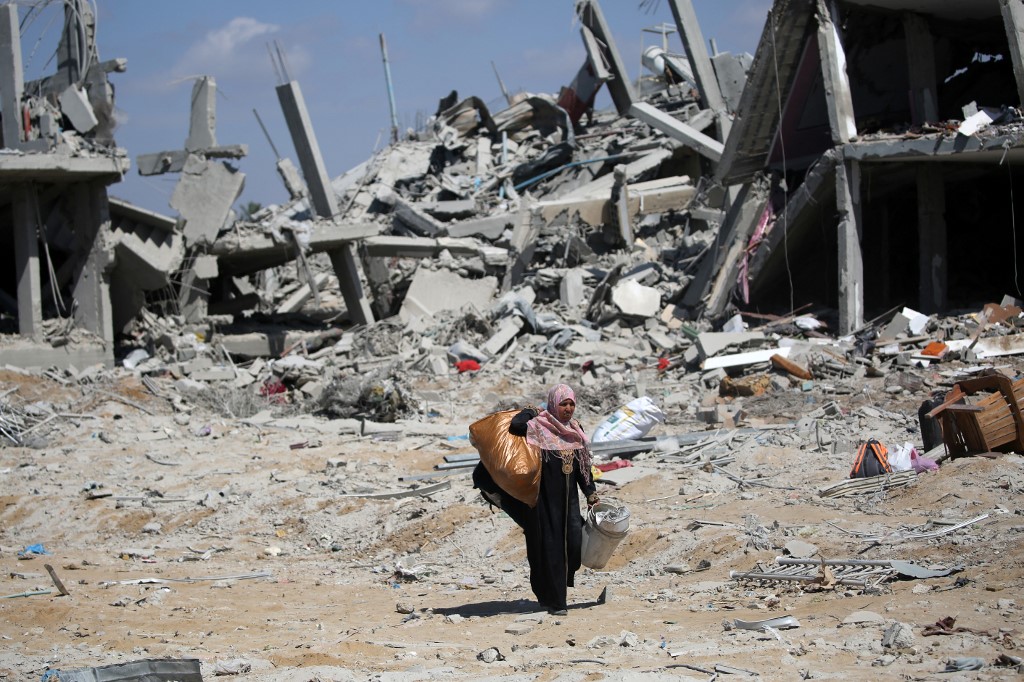 A Palestinian woman walks through the rubble in Deir al-Balah in the central Gaza Strip after an Israeli air strike, 29 August 2024 (Eyad Baba/AFP)