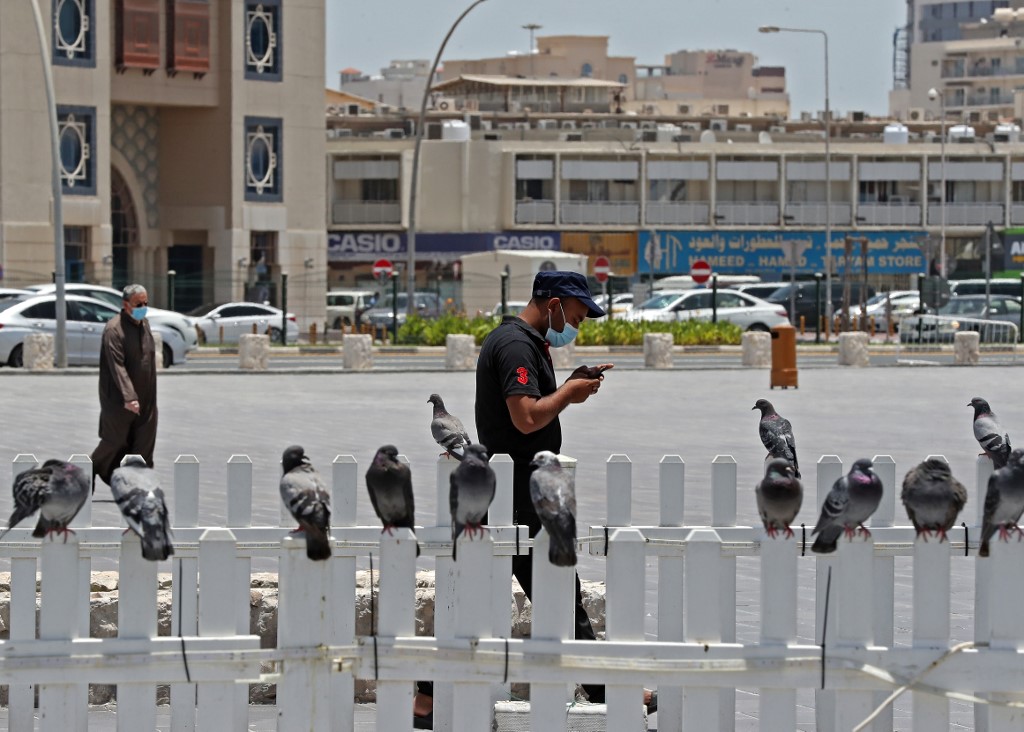 A man wearing a protective mask checks his phone as he walks by at Qatar's touristic Souq Waqif bazar in the capital Doha, on May 17, 2020,