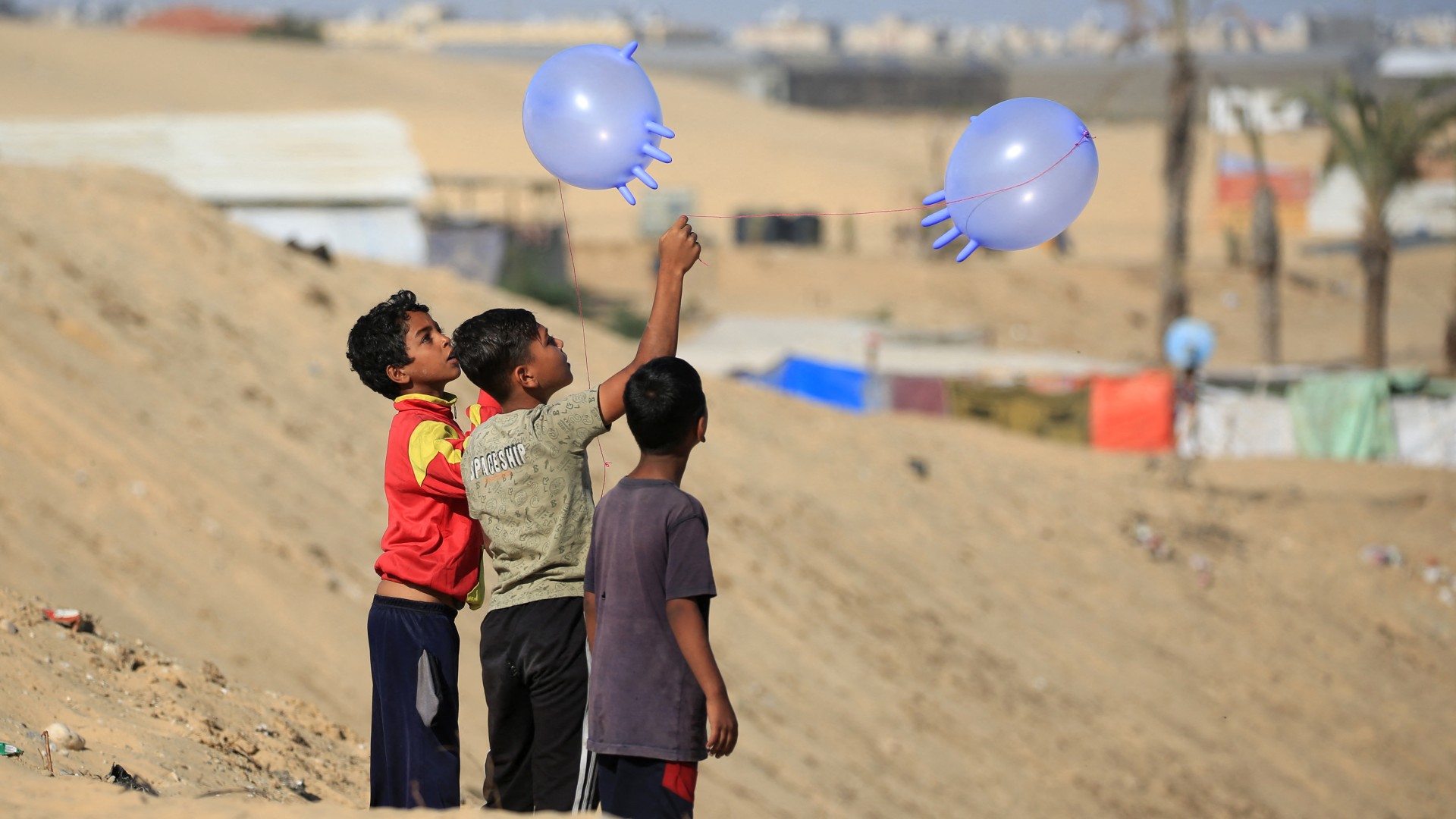 Displaced Palestinian children play with surgical rubber gloves in Rafah in the southern Gaza Strip, on 31 May (AFP/Eyad Baba)