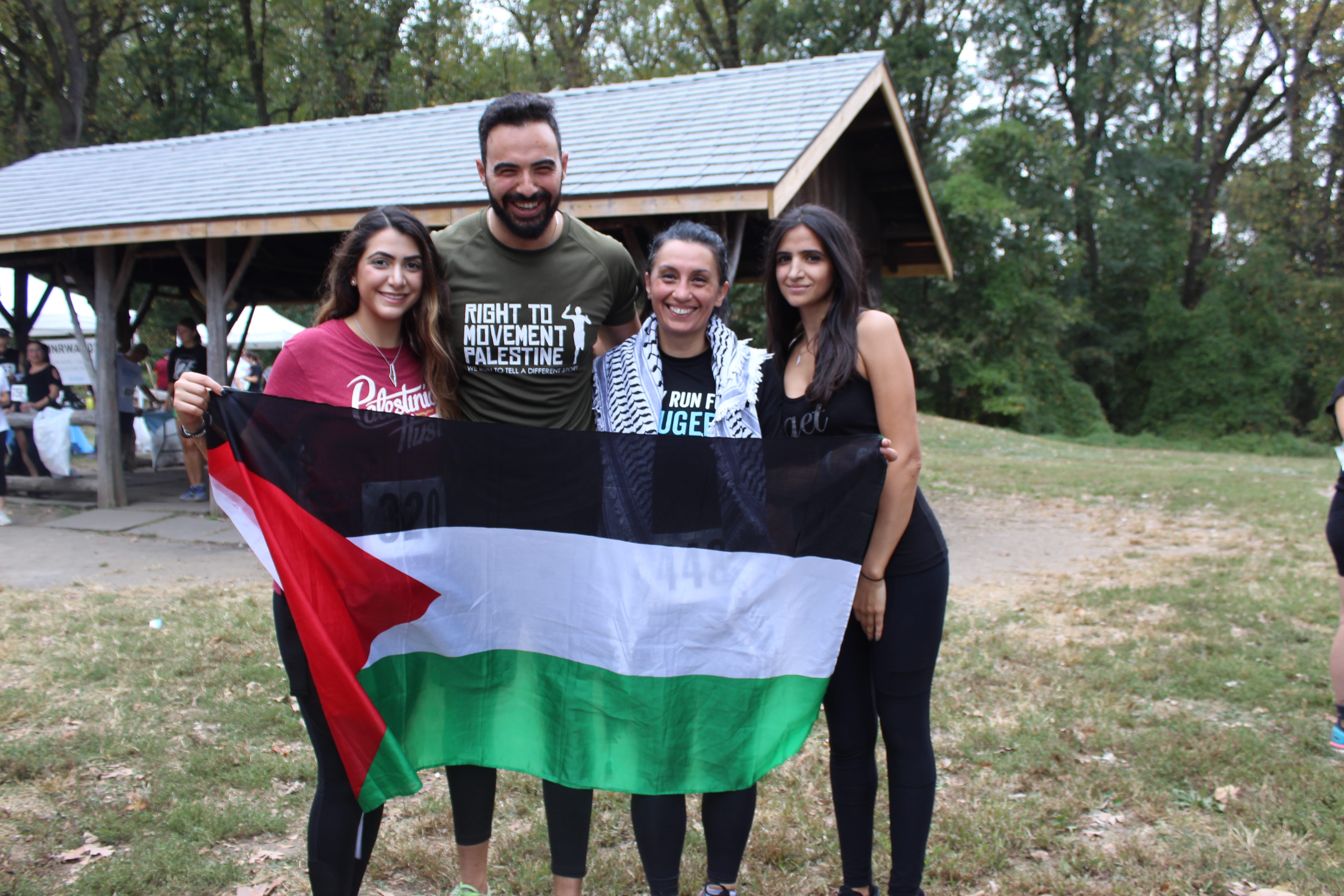 Rania Qawasma, with a kuffiyeh wrapped around her shoulders, holds up a Palestinian flag with three other runners who completed both races (MEE/Sheren Khalel