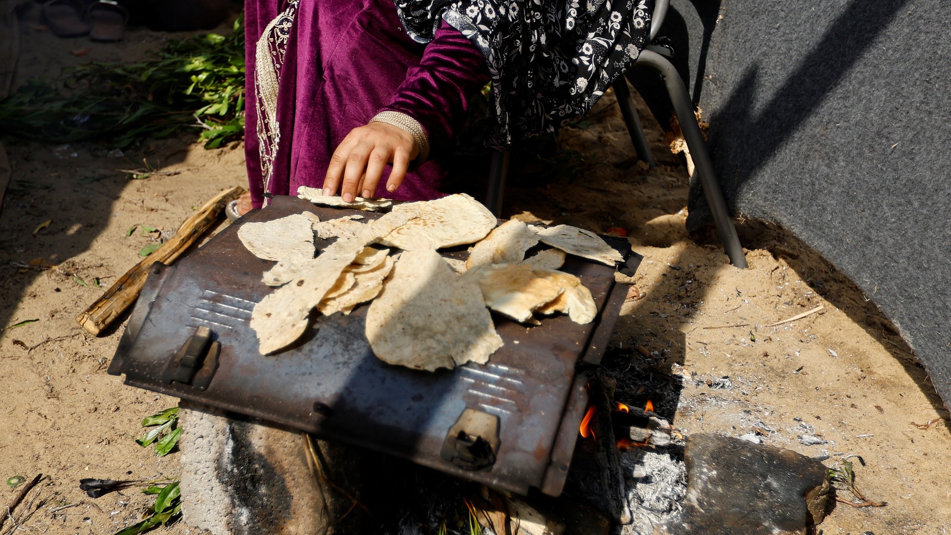 Une femme réchauffe des morceaux de pain dans un camp administré par l’ONU à Khan Younès, dans la bande de Gaza (Reuters)