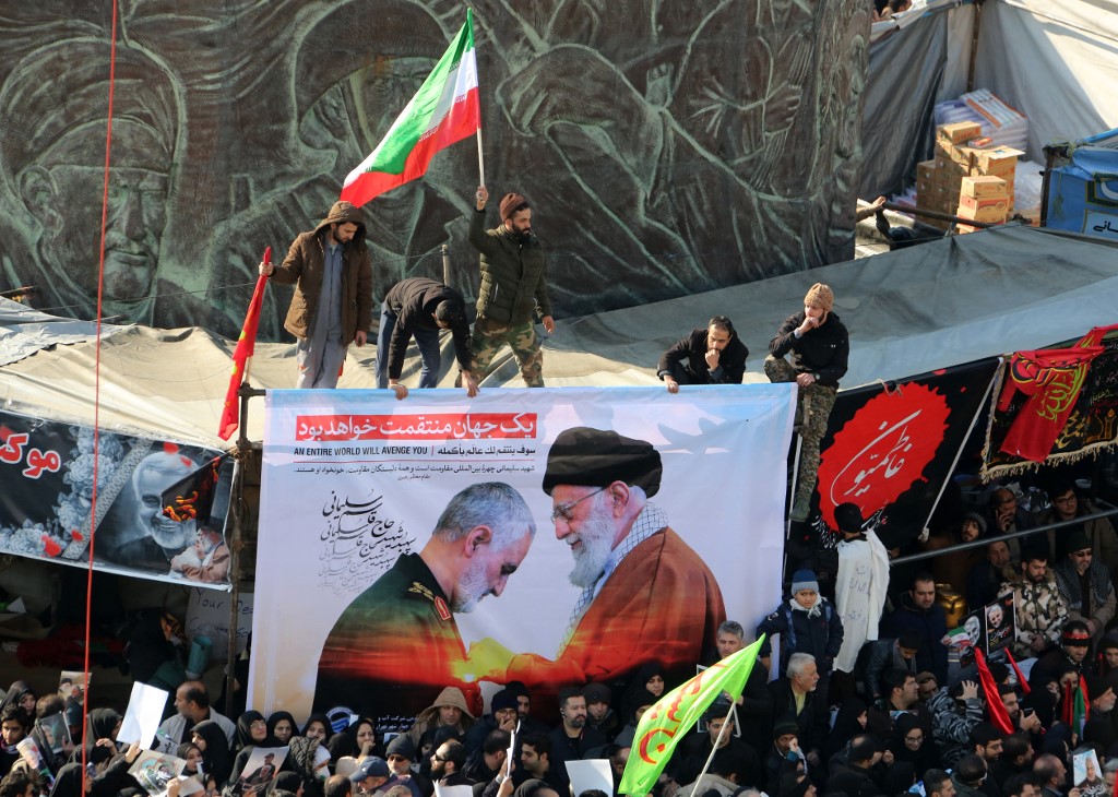 Iranian mourners carry a picture of Supreme Leader Ayatollah Ali Khamenei and General Qassem Soleimani during a funeral procession in Tehran on 6 January (AFP)