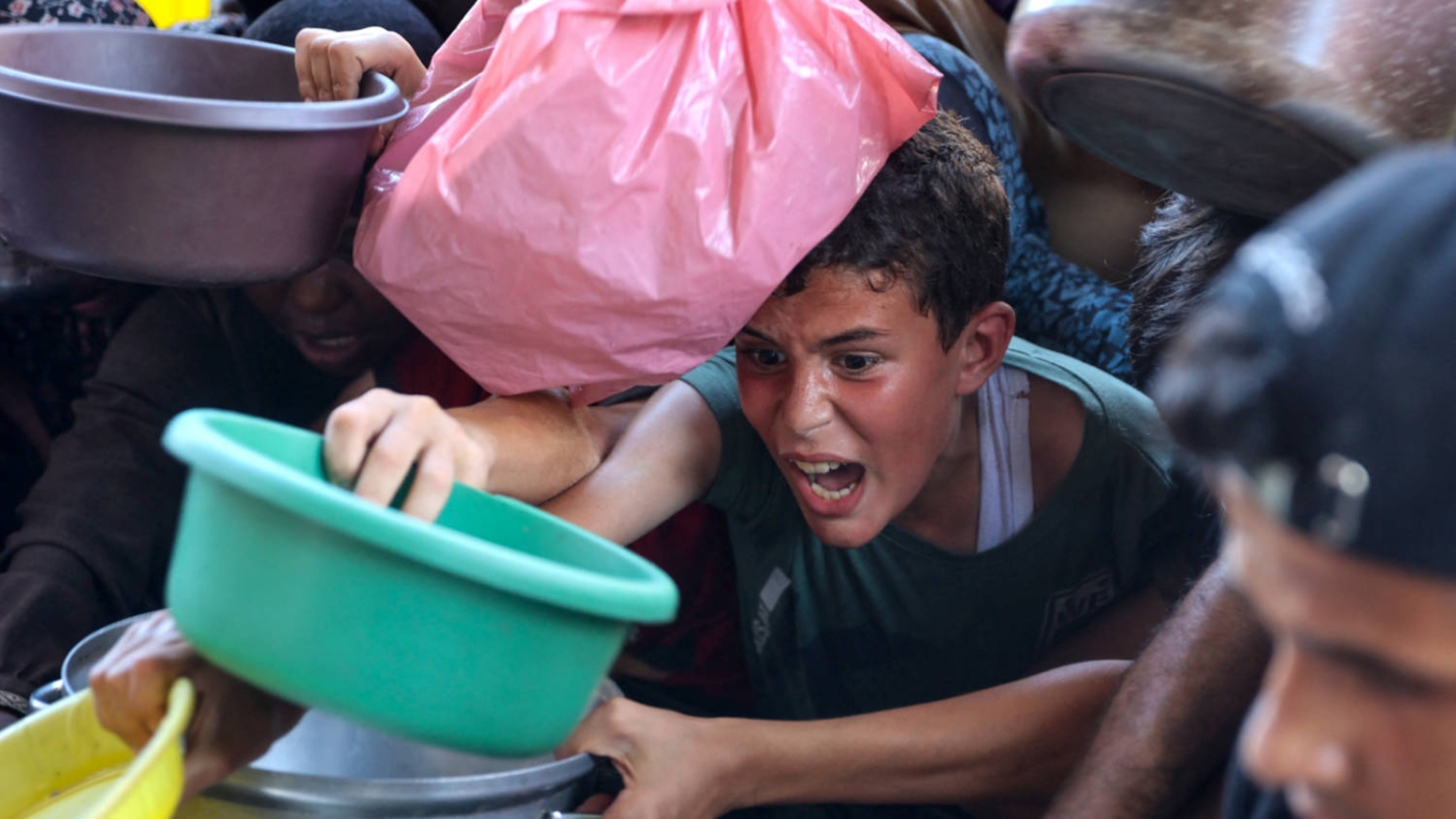 Homeless Palestinians wait to receive food at a distribution point in Beit Lahia, Gaza in July  2024