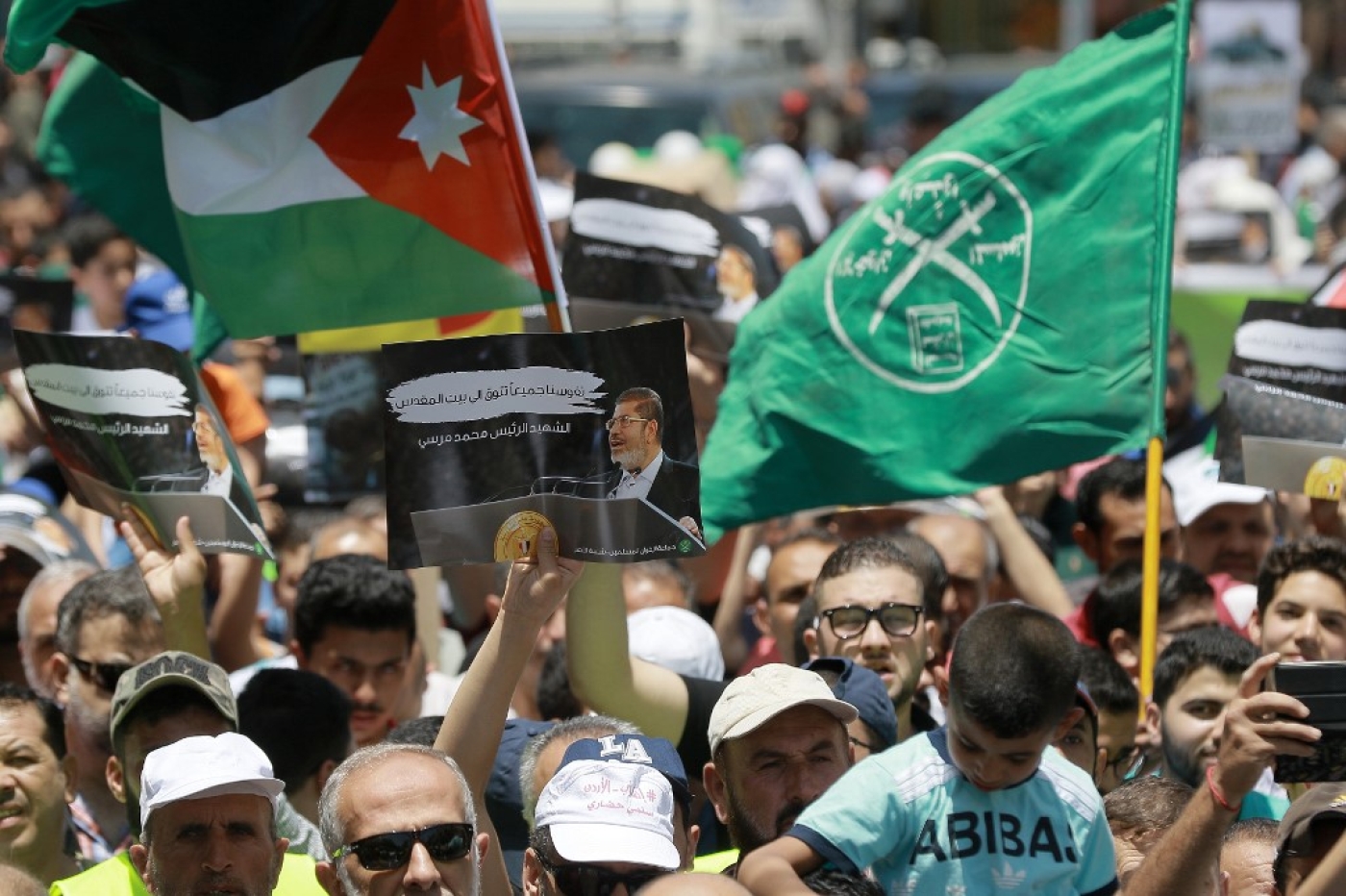Le drapeau de la Jordanie (à gauche) et des Frères musulmans (à droite) apparaissent à côté d’une pancarte en l’honneur du président égyptien déchu, Mohamed Morsi, lors d’une manifestation à Amman, le 21 juin 2019, contre l’« accord du siècle » de Donald Trump (AFP)