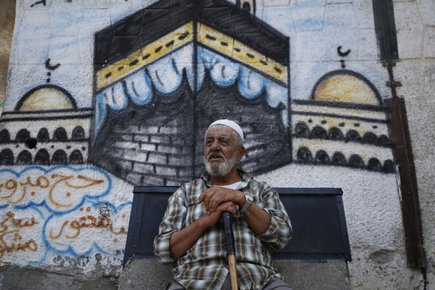 A Palestinian man sits in front of a mural paintings of the holy Kaaba,in Gaza City on 27 July 2020. (AFP)