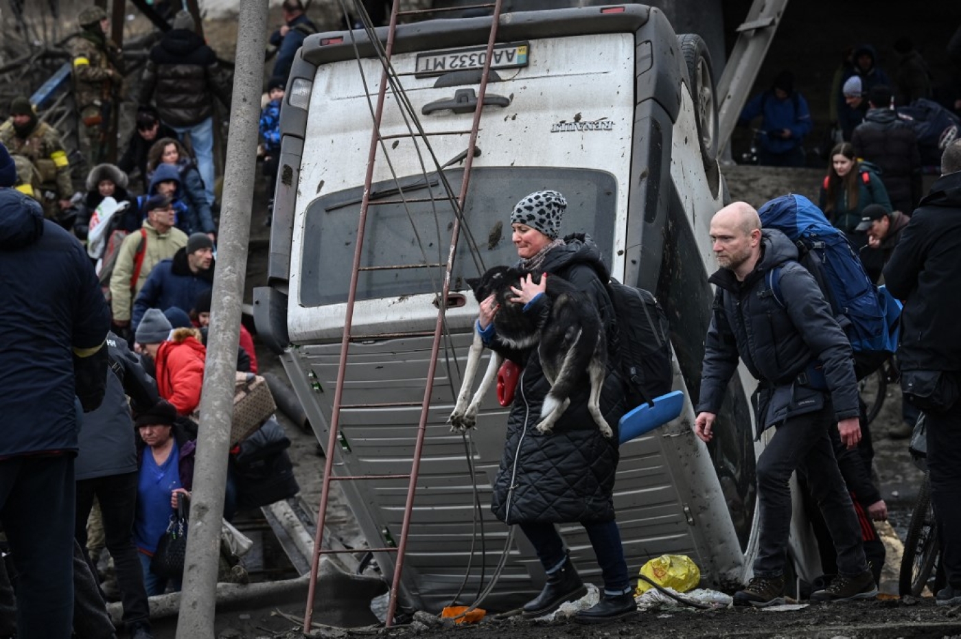 Une femme porte son chien tandis que des personnes traversent un pont détruit pendant l’évacuation de la ville d’Irpin, au nord-ouest de Kiev, lors de bombardements, le 5 mars 2022 (AFP/Aris Messinis)