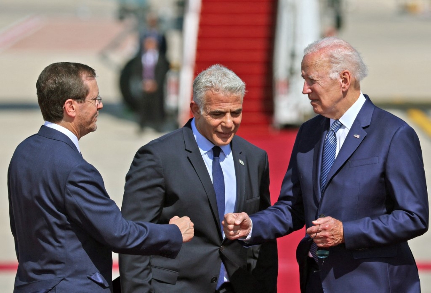 US President Joe Biden (R) bumps fists with Israel's President Isaac Herzog as caretaker Prime Minister Yair Lapid looks on, at Israel's Ben Gurion Airport in Lod near Tel Aviv, on 13 July 2022. (AFP)