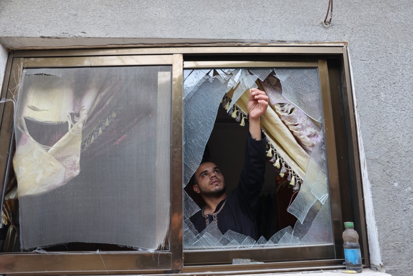 A Palestinian man removes glass shards from a broken window at his home which was damaged by Israeli air strikes in Rafah in the southern Gaza Strip, on 8 August 2022 (AFP)
