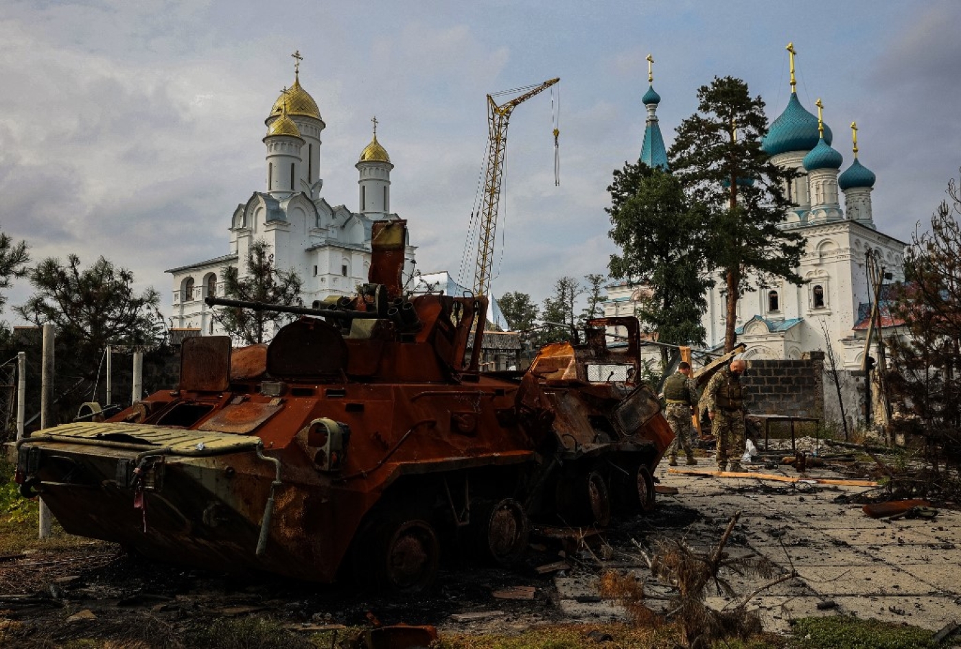 Photograph taken on 30 September 2022 shows Ukrainian servicemen walking next to a destroyed Russian Army APC in a yard of Burial Shroud of the Mother of God Orthodox Church on the bank of the Seversky Donets River near the town of Sviatohirsk, Donetsk region (AFP)