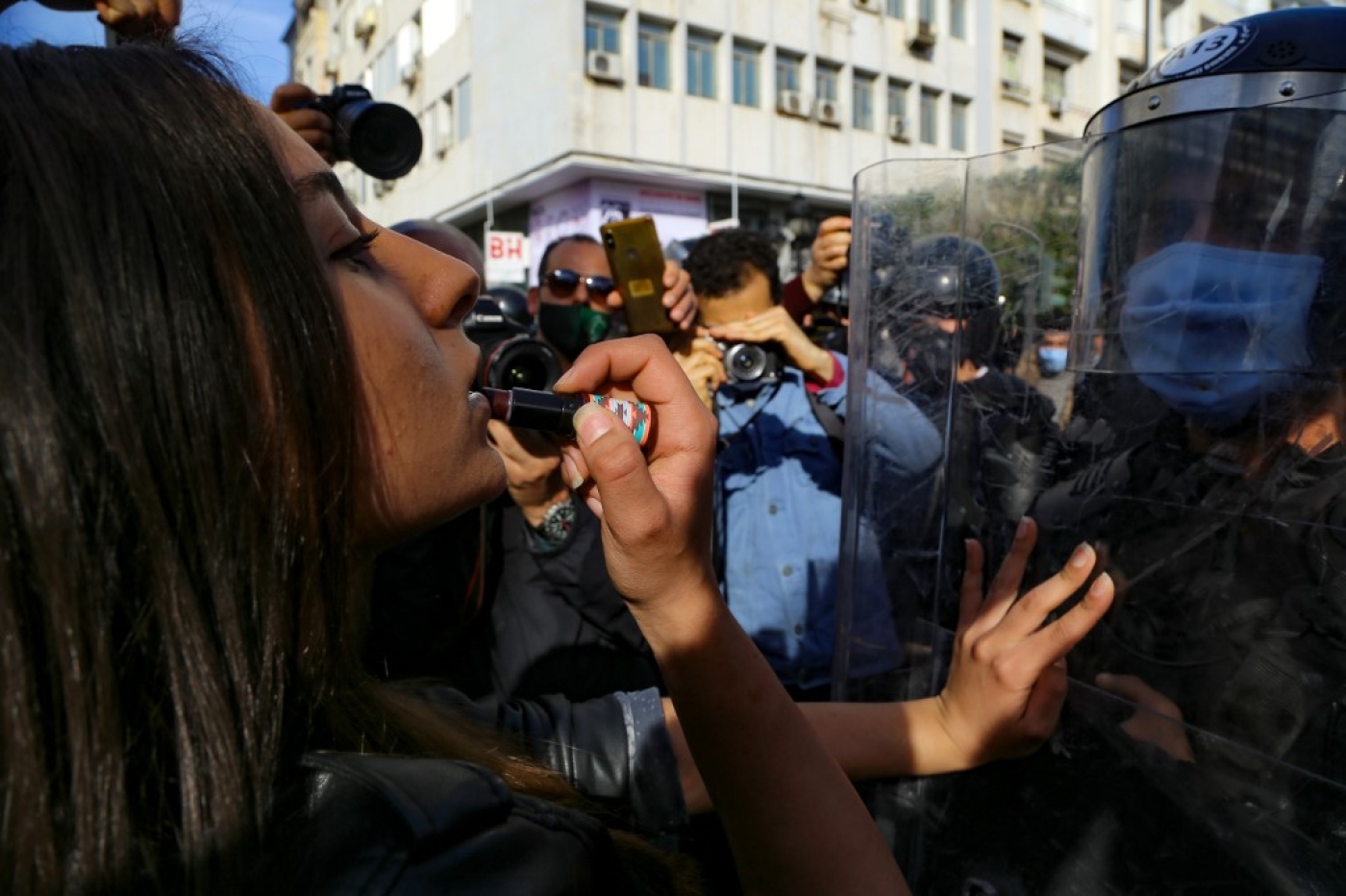 Une Tunisienne se remet du rouge à lèvres dans le reflet du casque d’un policier, lors de la manifestation du samedi 30 janvier, à Tunis (AFP)