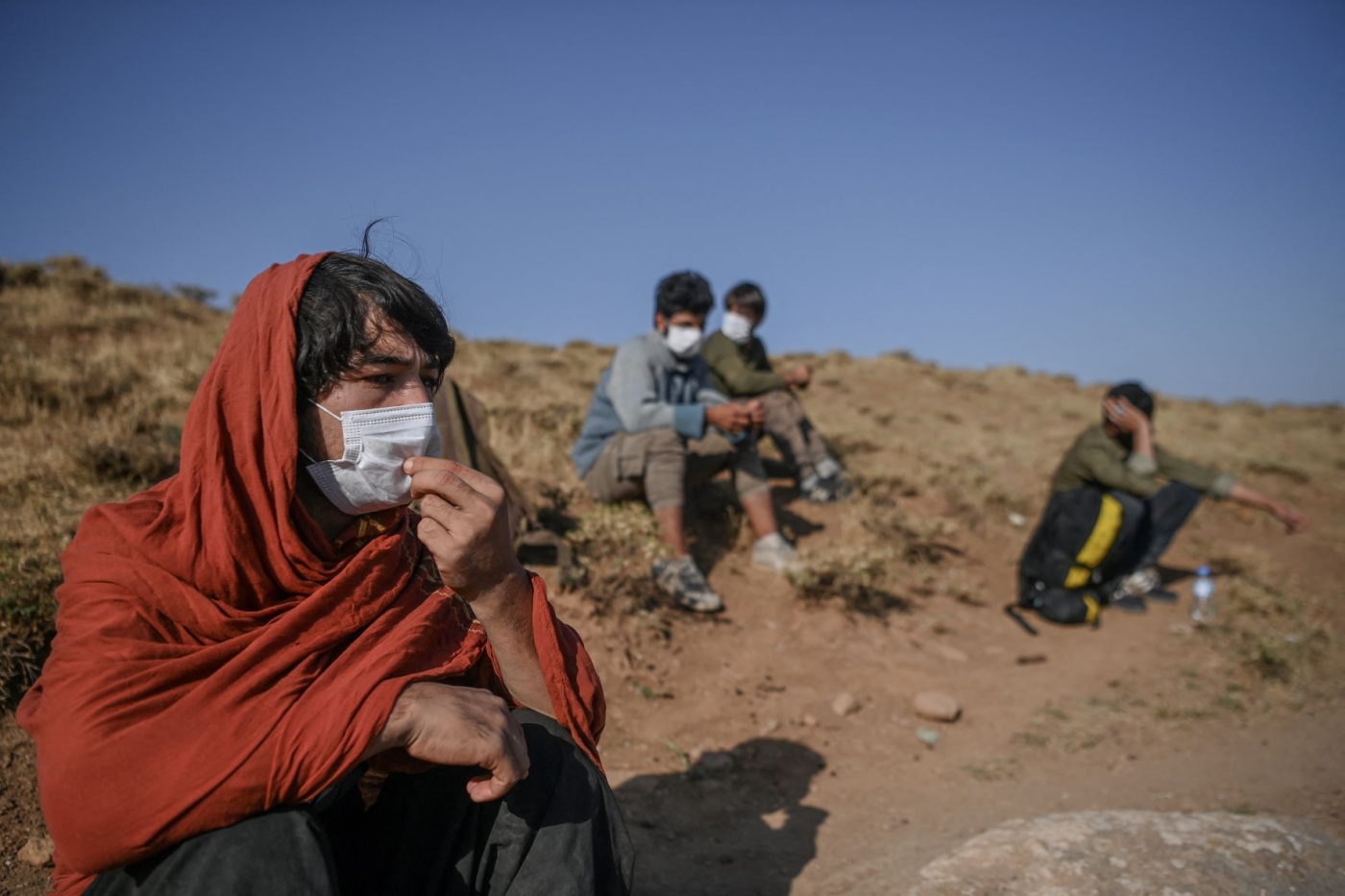 Afghan migrants rest while waiting for transport by smugglers after crossing the Iran-Turkish border in Tatvan, on the western shores of Lake Van, eastern Turkey, on 15 August 2021 (AFP)