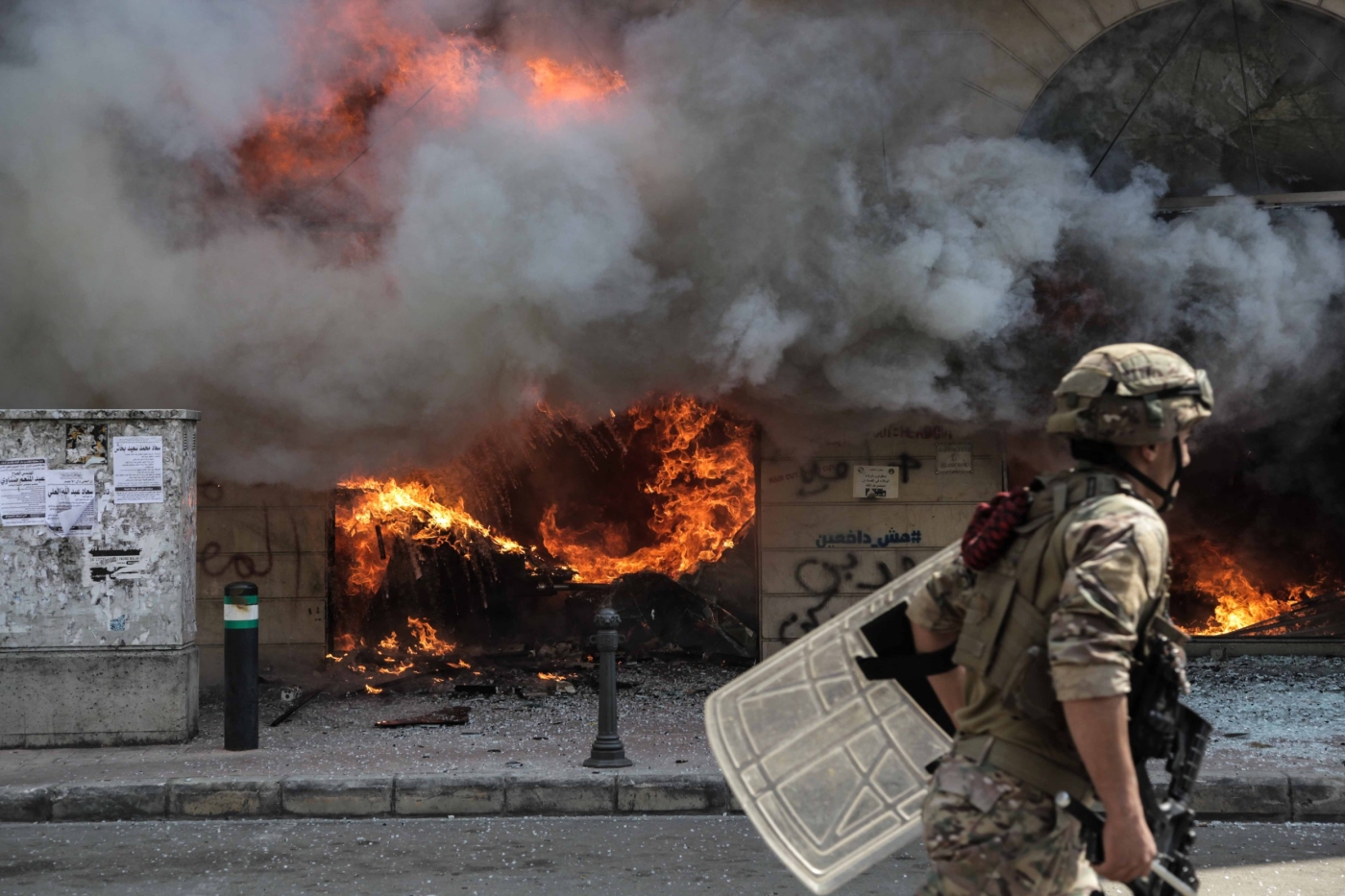A soldier walks past a burning bank branch in Tripoli, Lebanon on 28 April 2020, during protests following the death of Fawaz Fouad Samman, a 26-year-old demonstrator shot by the army the previous night (MEE/Elizabeth Fitt)