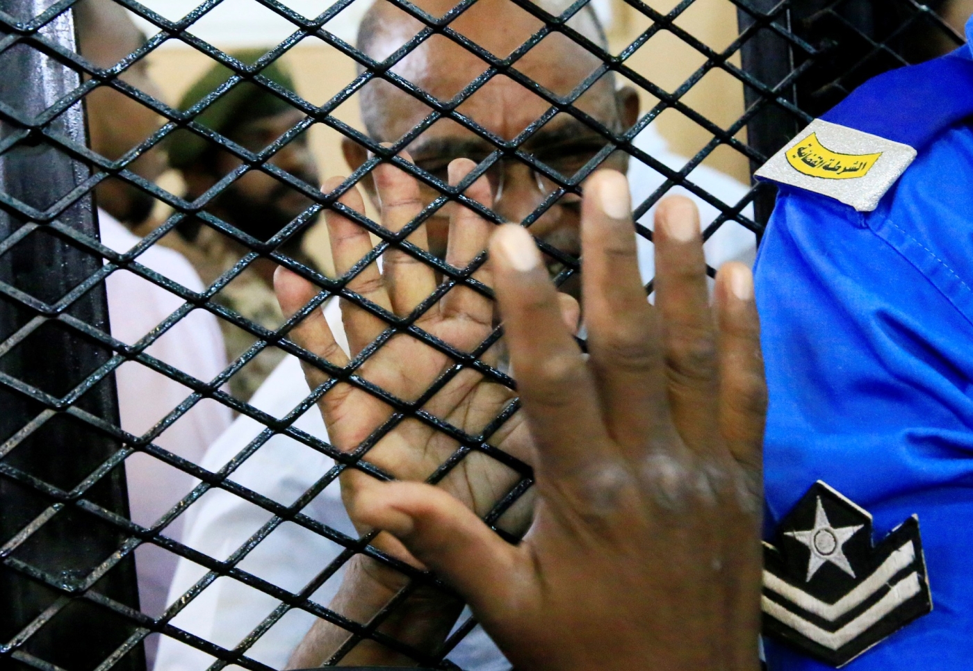 Omar al-Bashir greets a supporter from inside the defendant's cage during his trial in 2020 (Reuters)