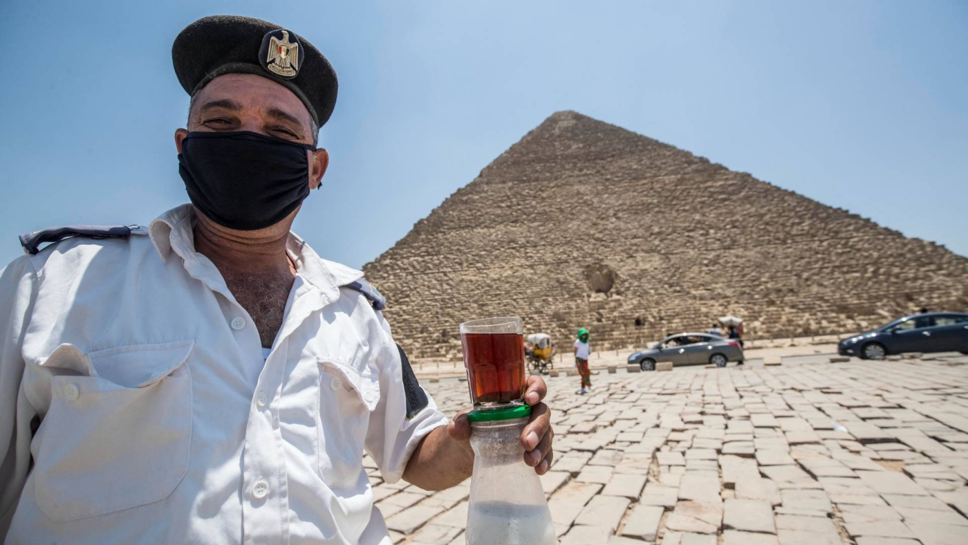 Un policier égyptien masqué en service à la nécropole des pyramides de Gizeh tient un verre de thé et un pot de sucre, le 1er juillet 2020 (AFP)