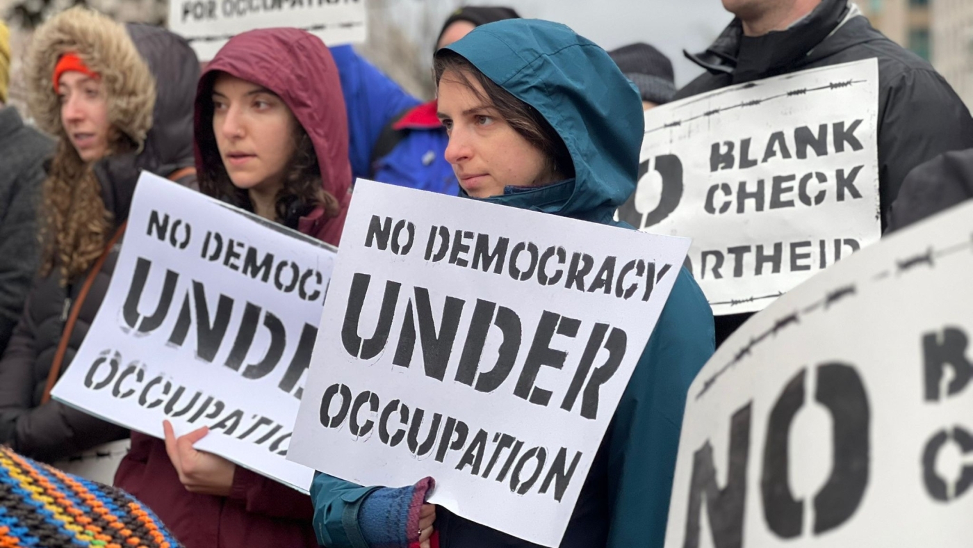 Protestors hold signs that say 'No Democracy Under Occupation' and 'No Blank Checks to Apartheid'.