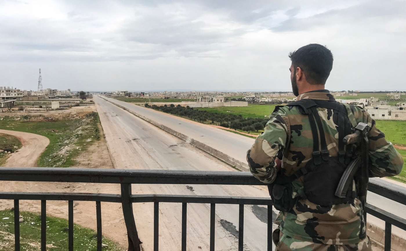 A Syrian army soldier stands overlooking a motorway 